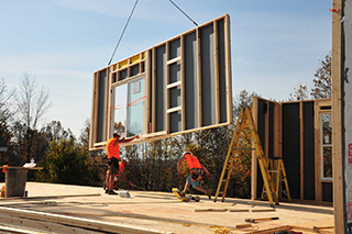 A wall panel is being lowered with construction workers placing it in position